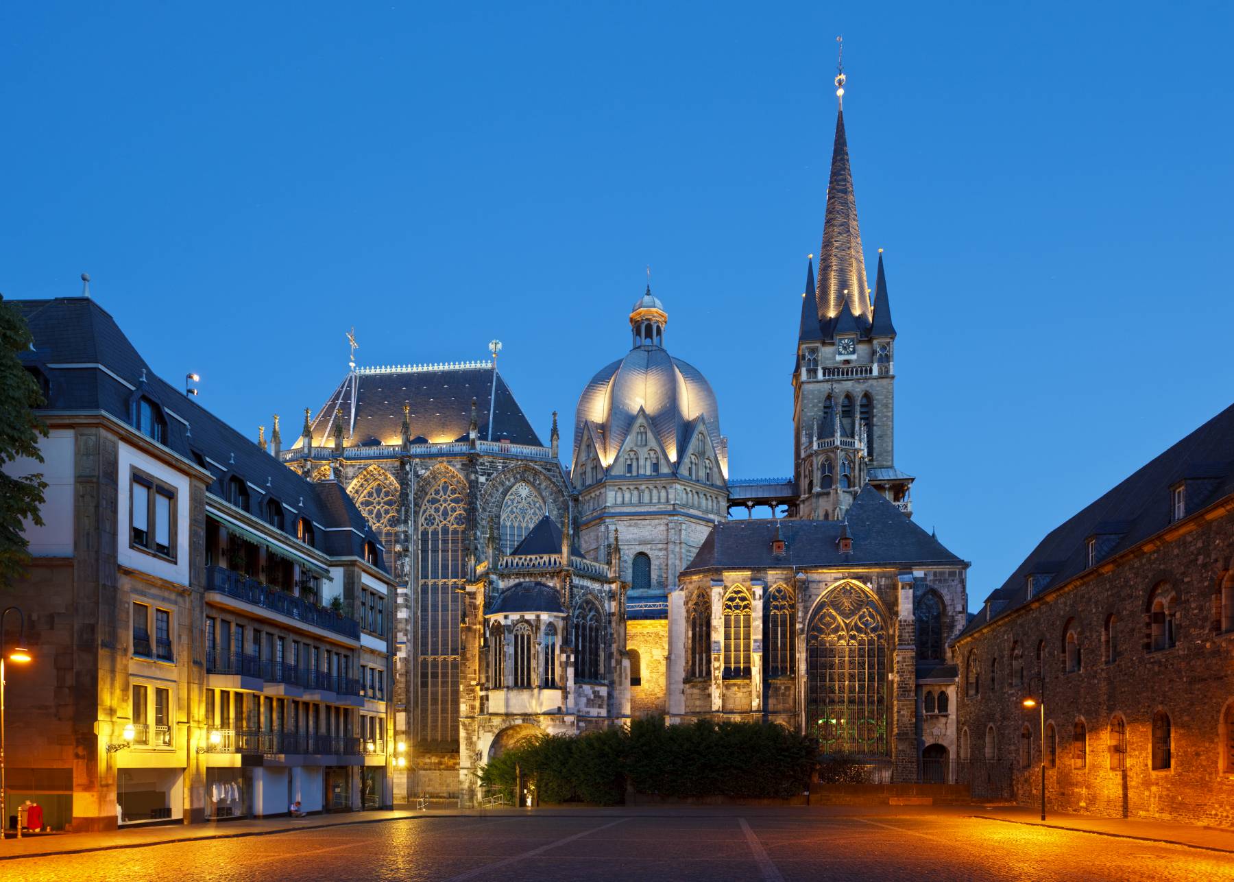 Aachener Dom bei Nacht, angestrahlt von orangem Licht mit dunkelblauem Himmel im Hintergrund