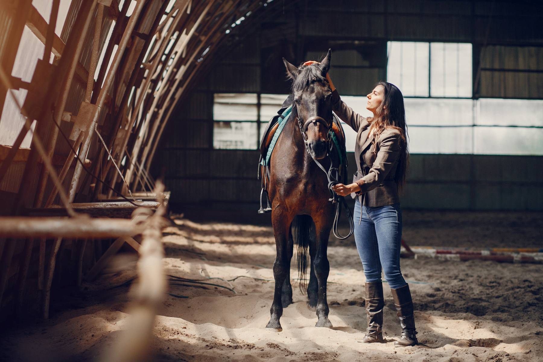 Eine Frau steht neben einem Pferd in einem Stall und streichelt es, während sie die Zügel in der Hand hält