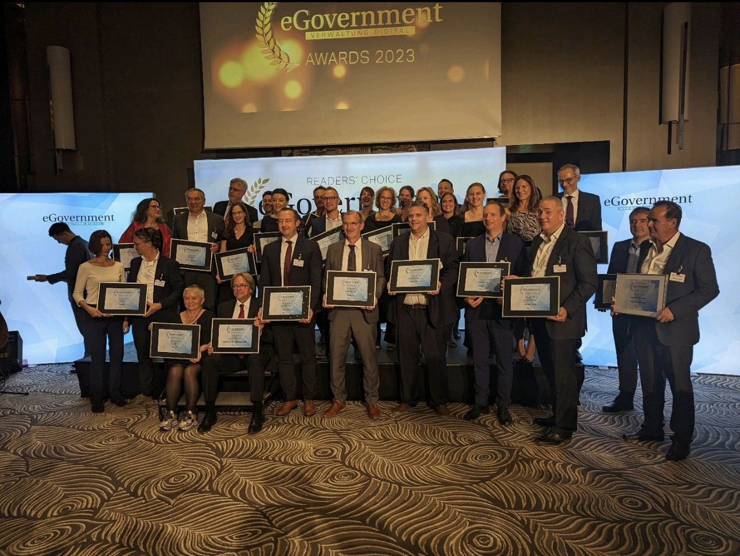 Alle Gewinner*innen des Readers Choice eGovernment Award stehen beieinander, schauen in die Kamera und halten ihren Rahmen mit der Auszeichnung vor sich.