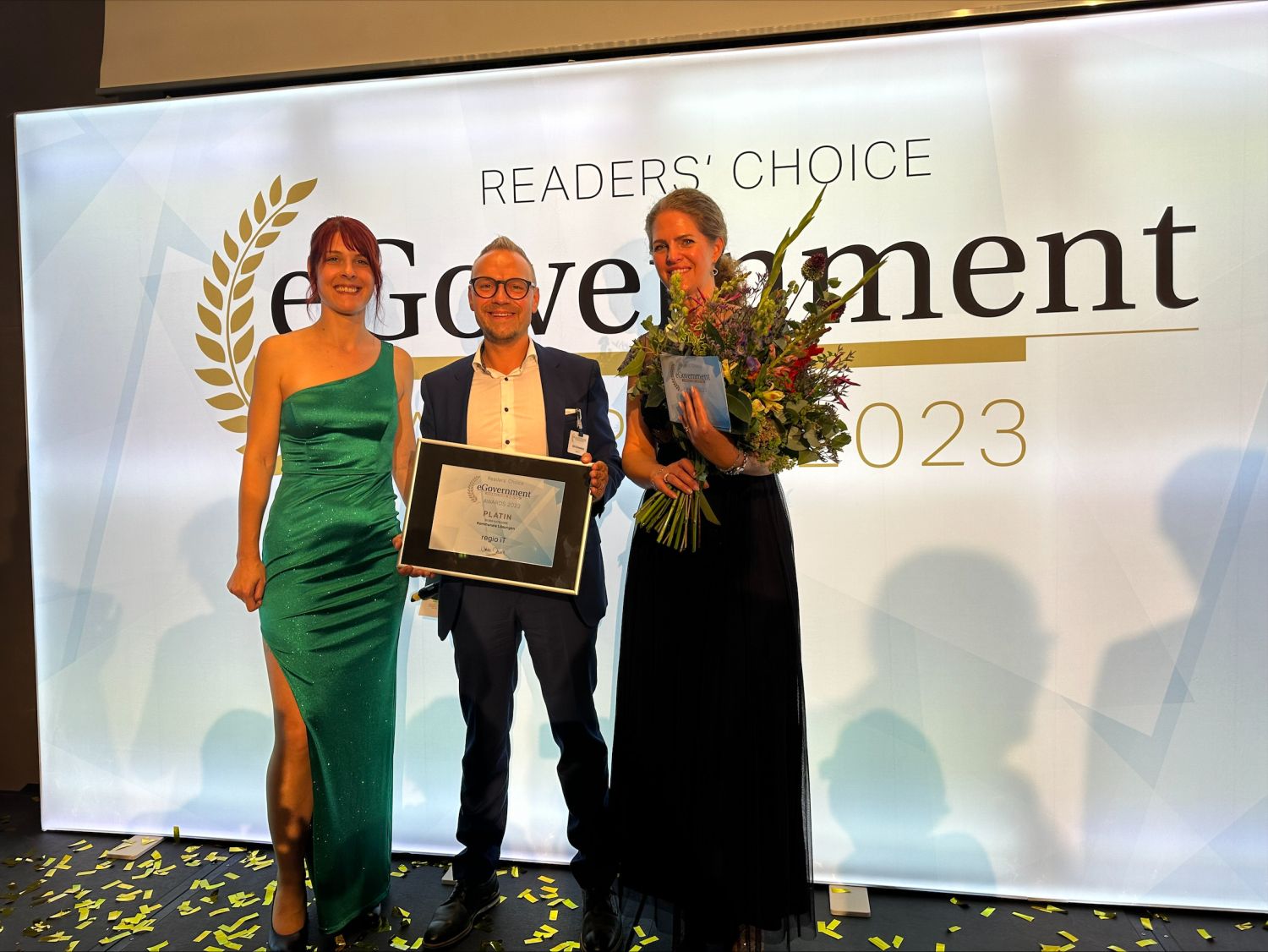 Dirk Schweikart hält einen Rahmen mit der Platinumauszeichnung in der Hand, rechts und links von ihm stehen zwei Damen in Abendkleidern, eine Dame hält einen Blumenstrauß.