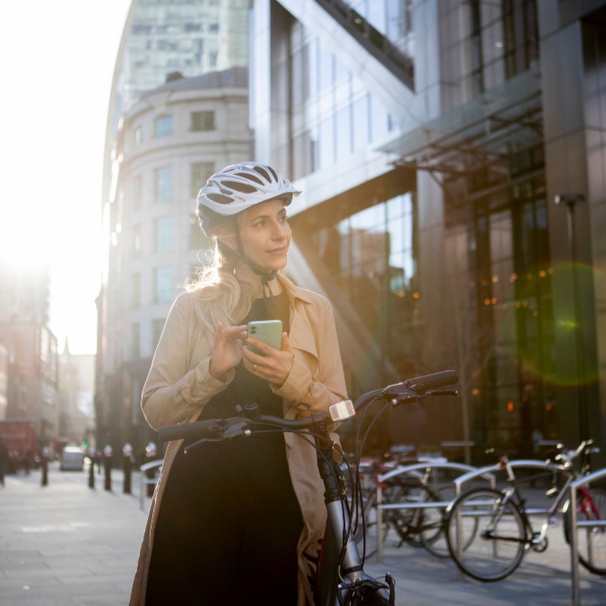 Eine Frau mit Fahrradhelm steht neben ihrem Fahrrad in der Stadt und hält ein Smartphone in der Hand