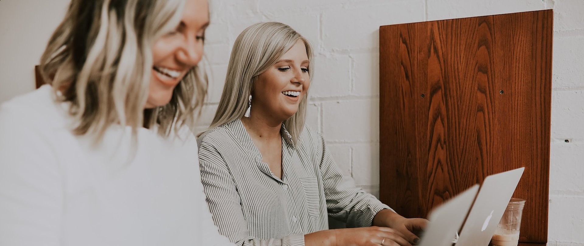 Zwei Frauen arbeiten lächelnd an ihren Laptops